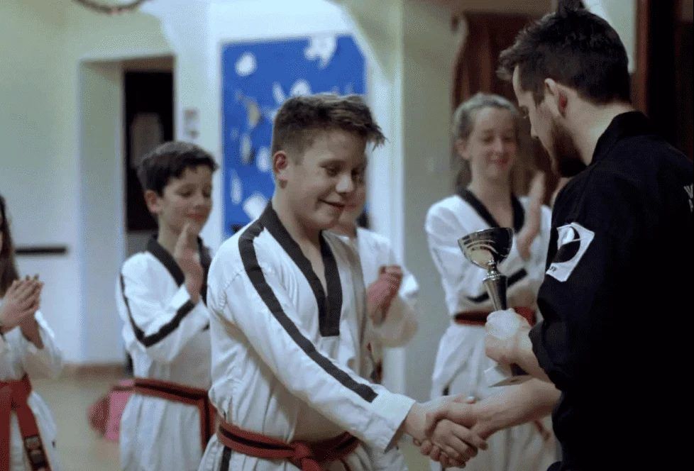 A student shaking hands with his instructor as he receives a trophy
